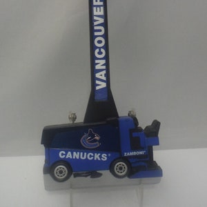 Könnte beinhalten: Ein blauer und weißer Eisschaber aus Plastik in Form eines Zamboni-Eisreinigungsfahrzeuges. Der Schaber trägt das Logo der Vancouver Canucks sowie die Worte "Zamboni" und "Canucks".