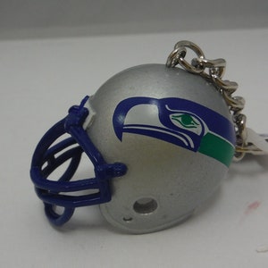 May include: A silver football helmet keychain with a blue and green Seattle Seahawks logo. The helmet has a blue facemask.