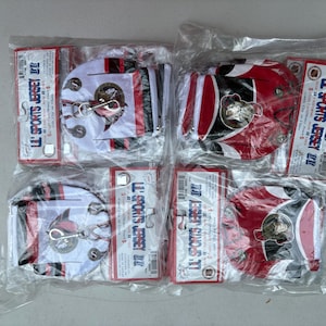 May include: Four hockey jersey keychains in plastic packaging. The keychains are red, white, and black with a team logo. Each package includes a red and white tag with the text "LL SPORTS JERSEY".