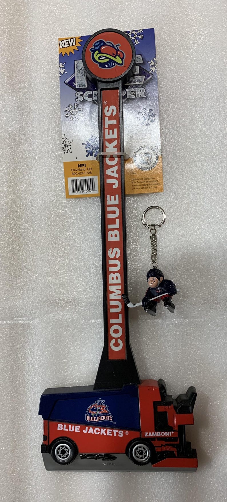 Puede incluir: Un abrebotellas con el tema de los Columbus Blue Jackets con un llavero de un jugador de hockey. El abridor tiene un dise&ntilde;o rojo y negro con el logotipo del equipo y las palabras "COLUMBUS BLUE JACKETS". El llavero presenta un jugador de hockey.