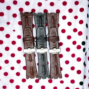 May include: Three watch straps, one brown, one black, and one brown, with white stitching. The straps are on a white background with red polka dots.
