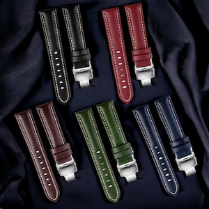 May include: Six pairs of leather watch straps in different colors, including black, red, brown, green, and blue. Each strap has white stitching and a silver buckle.