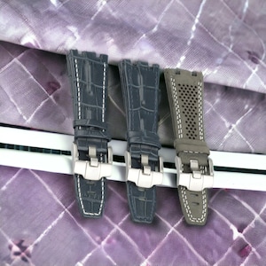 May include: Three watch straps in different styles. The straps are all black with white stitching. The strap on the left has a crocodile pattern, the middle strap has a crocodile pattern, and the strap on the right has a perforated pattern.