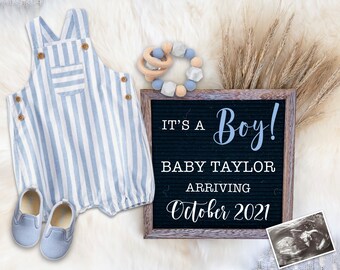 May include: A chalkboard sign with the text "It's a Boy! Baby Taylor Arriving October 2021". A blue and white striped baby onesie, a pair of blue baby shoes, a wooden ring toy, and a beaded necklace are arranged around the sign. A black and white ultrasound image is in the bottom right corner.