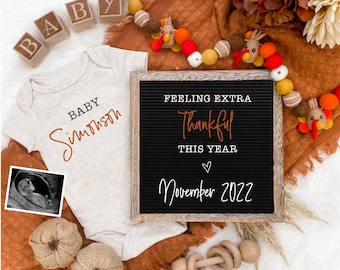 Peut inclure: Une grenouillère bébé marron et blanche avec le texte "Baby [name]" dessus. Un bloc de lettres épellant "BABY" est sur le côté gauche de la grenouillère. Un tableau noir avec le texte "Feeling extra thankful this year November 2022" est sur le côté droit de la grenouillère. Une petite image d'échographie est sur le côté gauche de la grenouillère. Une couverture marron et blanche est derrière la grenouillère. Une guirlande de dindes et de boules en feutre est en haut de l'image.