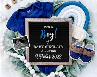 May include: A blue baby onesie, a black letter board with the text "It's a Boy! Baby Sinclair Arriving October 2022", a blue and white rainbow, and a pair of brown and blue baby shoes on a green leafy background.