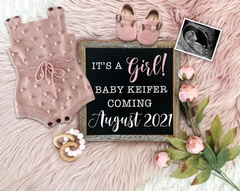 Puede incluir: Un pelele de punto rosa para bebé con un lazo, un par de zapatos de bebé rosas, un mordedor de madera para bebé, un letrero de pizarra enmarcado que dice "It's a Girl! Baby Keifer Coming August 2021", y un ramo de flores rosas sobre una superficie rosa peluda.