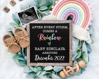 May include: A wooden letter board with the text "After every storm, comes a rainbow" in colorful letters. Below the text is "Baby Sinclair arriving December 2022". The board is surrounded by a green wreath, a rainbow yarn wall hanging, a pair of brown baby shoes, and a wooden rattle.