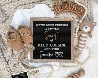 May include: A black letter board with the text "We've been keeping a little secret...♡ Baby Collins arriving December 2022". The board is surrounded by a white blanket, a white onesie, brown baby shoes, a wooden toy, a crocheted bear toy, and a white beaded garland.