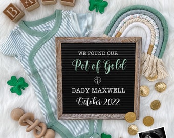 May include: A green and white striped baby onesie with a green shamrock and the words "We found our Pot of Gold Baby Maxwell October 2022" on a black letter board.