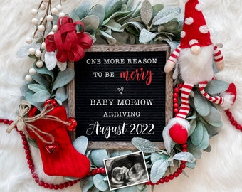 May include: A Christmas-themed pregnancy announcement with a chalkboard sign that reads "One more reason to be merry. Baby Moriow arriving August 2022". The sign is surrounded by a green wreath with red berries and a red and white gnome.