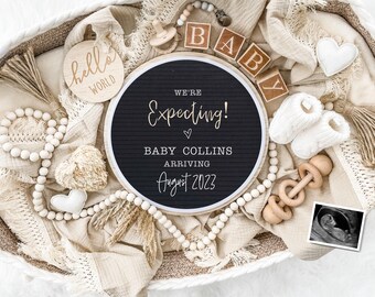 May include: A black and white letter board with the text "We're Expecting! Baby Collins Arriving August 2023" surrounded by a white beaded garland, wooden blocks spelling "BABY", a wooden rattle, a white baby bootie, a white heart, and a small ultrasound image.
