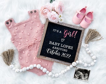 Puede incluir: Un mono de bebé de punto rosa con lunares blancos, un tablero de letras con el texto "It's a Girl! Baby Lopez Arriving October 2022", un par de zapatos de bebé rosas, una guirnalda de cuentas blancas con borlas marrones y una imagen de ultrasonido en blanco y negro.