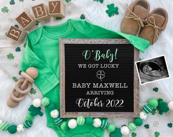 May include: A green baby onesie with a letter board that reads "O' Baby! We got lucky. Baby Maxwell arriving October 2022". There are green shamrocks, a wooden rattle, and brown baby shoes in the image.