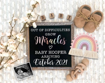 May include: A pregnancy announcement with a black letter board that reads "OUT OF DIFFICULTIES GROW Miracles BABY HOOPER ARRIVING October 2021." The image includes baby shoes, a rainbow decoration, wooden blocks spelling "BABY," and a sonogram.