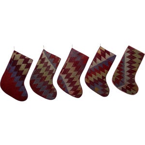 May include: Five Christmas stockings with a geometric diamond pattern in shades of red, tan, and blue. Each stocking has a loop for hanging. The stockings are arranged in a row against a white background.