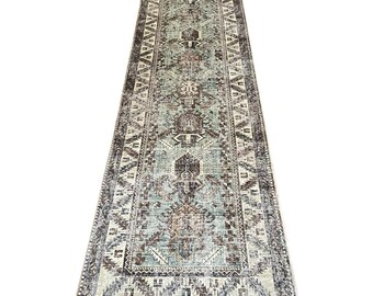 May include: A long, rectangular rug with a distressed, vintage appearance. The rug features a central design in shades of teal, brown, and cream, with geometric patterns and a border in darker tones. The rug is suitable for a hallway or entryway.