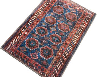 May include: Rectangular rug with a central blue field featuring geometric patterns in red, black, and brown. The rug has a detailed border with alternating stripes and a repeating design. The overall aesthetic is traditional and ornate.
