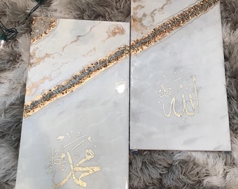 May include: Two white canvas paintings with gold accents and Arabic calligraphy. The left painting features the word "Muhammad" in gold script. The right painting features the word "Allah" in gold script.
