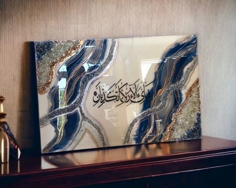 May include: A rectangular resin art piece with a white background and blue and gold abstract swirls. The art piece features Arabic calligraphy in black.