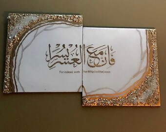 May include: Two white canvases with gold accents and glitter. The canvases are joined together and feature Arabic calligraphy and the text "For indeed, with hardship will be ease."