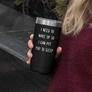 May include: A black stainless steel tumbler with a white inscription that reads "I need to wake up so I can put you to sleep".