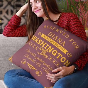 May include: A maroon throw pillow with gold text that reads "Reserved for Diana Washington The World's Greatest Fan". The pillow has a gold star design and a football graphic.