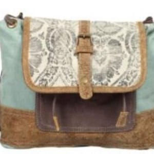 May include: A canvas messenger bag with a flap closure. The bag features a light blue body, a brown bottom, and a flap with a cream-colored floral pattern. The bag has a brown leather strap and buckle closure. The bag has a front pocket.