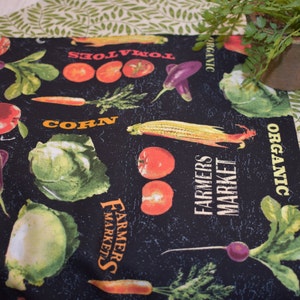 May include: Black fabric with a white and yellow print of vegetables and the words "Farmers Market" and "Organic".