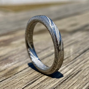 May include: A silver ring with a unique, swirling pattern. The ring is made of metal and has a polished finish.