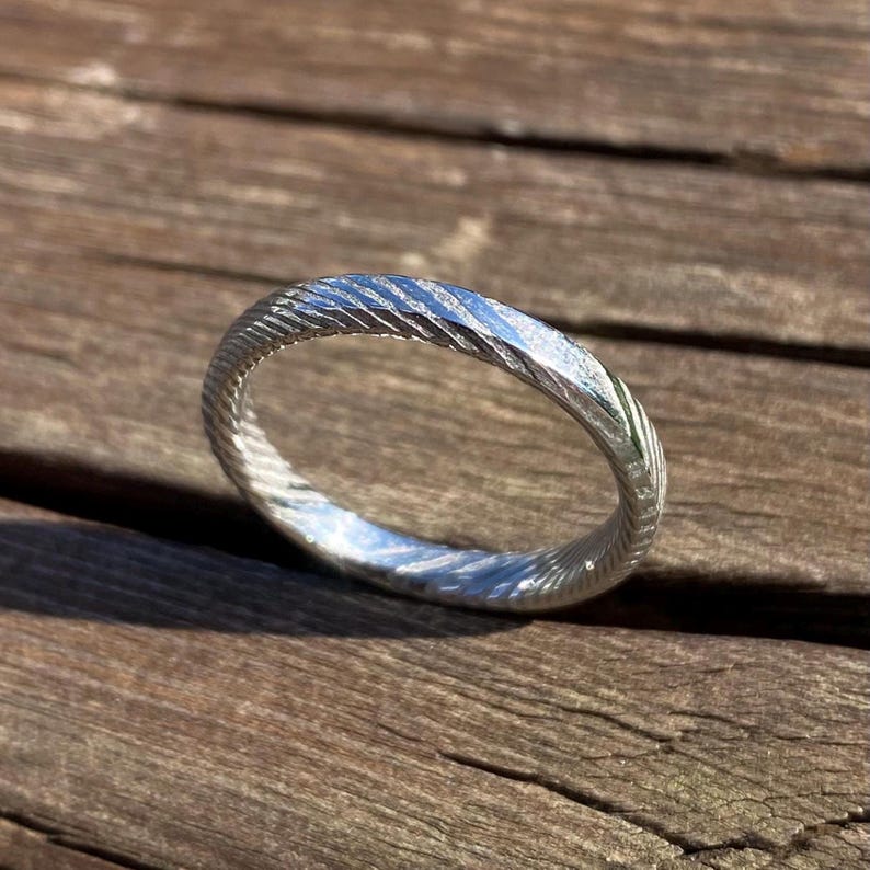 May include: A silver ring with a textured, grooved design. The ring is made of metal and has a polished finish.