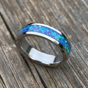 May include: A silver ring with a vibrant blue opal inlay. The opal displays shades of blue and green, set within a polished silver band. The ring is shown on a wooden surface, highlighting its reflective qualities.