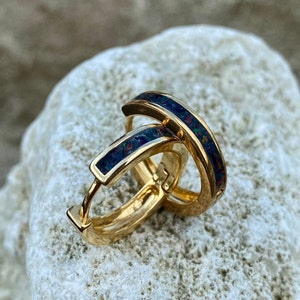 Op de afbeelding: Een paar gouden creolen met een zwarte en iriserende opaal inlay. De oorbellen zijn simpel en elegant.
