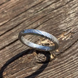May include: A silver ring with a textured, hammered finish. The ring is simple and elegant, with a polished, smooth interior.