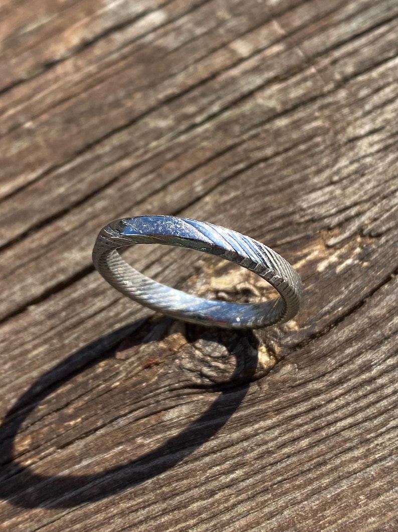 May include: A silver ring with a textured, hammered finish. The ring is simple and elegant, with a polished, smooth interior.