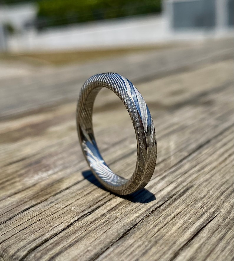 May include: A silver ring with a unique, swirling pattern. The ring is made of metal and has a polished finish.