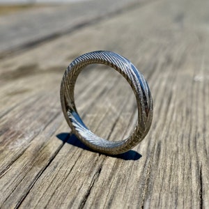 May include: A silver ring with a textured, swirling pattern. The ring is made of metal and has a polished finish.