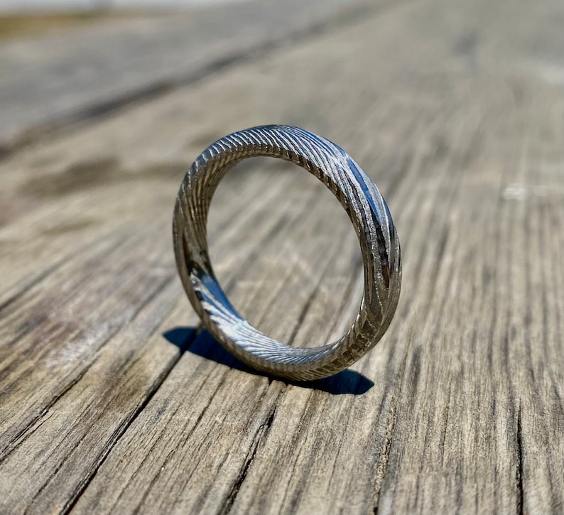 May include: A silver ring with a textured, swirling pattern. The ring is made of metal and has a polished finish.