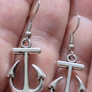 Puede incluir: Un par de pendientes colgantes de metal plateado con forma de ancla. Cada pendiente presenta un diseño de ancla náutica clásica suspendido de un sencillo gancho de metal plateado, con un acabado metálico pulido y una estructura sólida y resistente.