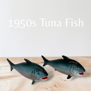 Könnte beinhalten: Ein Paar vintage Keramik-Salz- und Pfefferstreuer in Form von Thunfischen. Die Streuer sind blau und grau mit roten Mündern. Die Streuer stehen auf einer Holzoberfläche. 1950s Tuna Fish