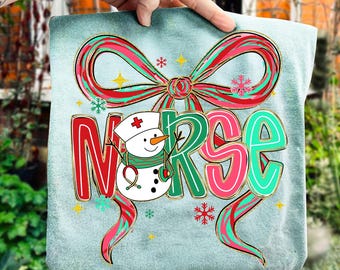 Könnte beinhalten: Hellblaues Kissen mit dem Wort "NURSE" in großen, farbenfrohen Buchstaben. Ein Schneemann mit Krankenschwestermütze und Stethoskop ist im Design abgebildet, zusammen mit einer rot-grünen Schleife und Schneeflocken.
