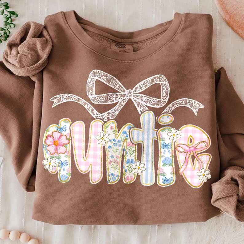 K&ouml;nnte beinhalten: Ein braunes Sweatshirt mit einem floralen Design, das "Auntie" sagt, mit einer wei&szlig;en Schleife aus Spitze oben drauf.