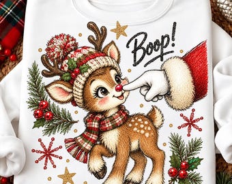 May include: A white sweatshirt featuring a graphic of a brown reindeer wearing a red and white knit hat and a plaid scarf. A gloved hand touches the reindeer's red nose, with the text Boop! above. The design includes pine branches, holly, and stars.