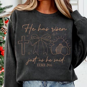 May include: A black sweatshirt with a brown graphic design that says "He has risen just as he said. LUKE 24:6". The graphic includes a cross, a bow, and a tomb.