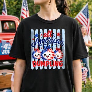 Op de afbeelding: Zwart T-shirt met een patriottisch ontwerp. Het ontwerp bevat de tekst "all American Dumpling" in rood, wit en blauw, en drie lachende dumpling-personages versierd met sterren en strepen. Het T-shirt is een casual stijl.