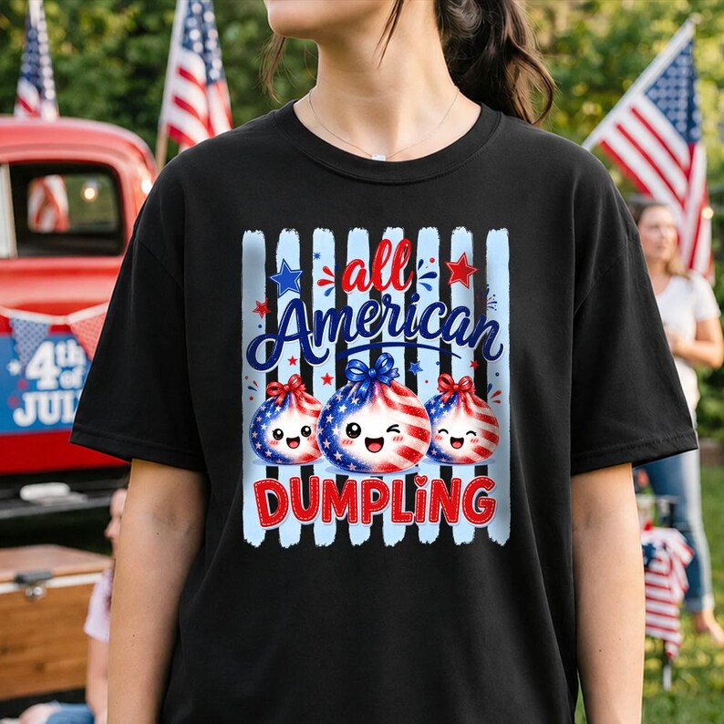Op de afbeelding: Zwart T-shirt met een patriottisch ontwerp. Het ontwerp bevat de tekst "all American Dumpling" in rood, wit en blauw, en drie lachende dumpling-personages versierd met sterren en strepen. Het T-shirt is een casual stijl.