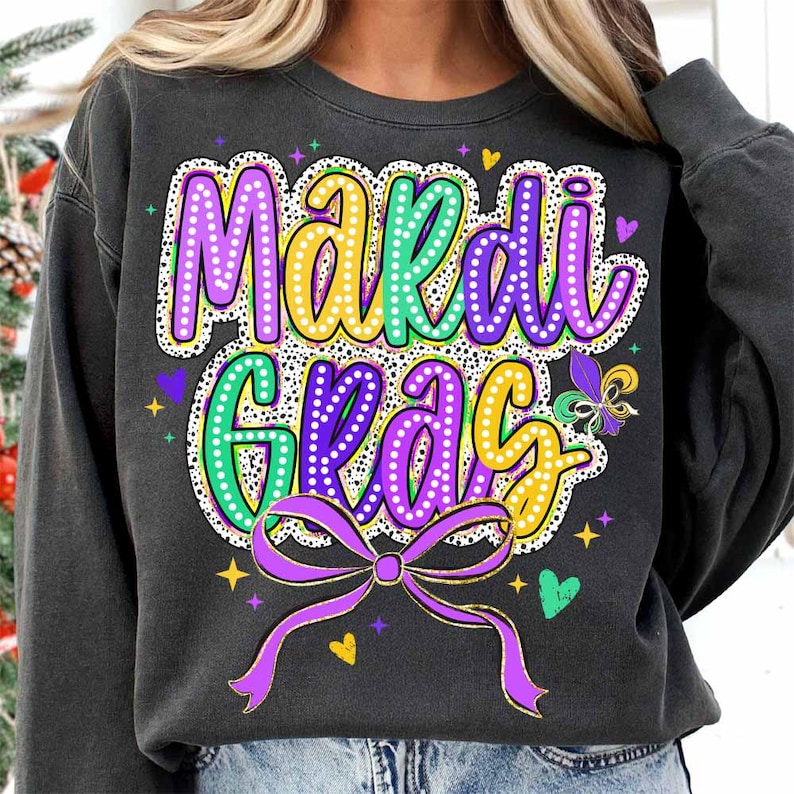 May include: A black sweatshirt with a purple, green and yellow Mardi Gras design. The design features the words "Mardi Gras" with a purple bow and gold glitter accents.