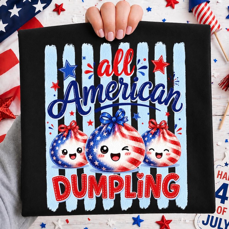 Op de afbeelding: Zwart T-shirt met een patriottisch ontwerp. Het shirt heeft de tekst "All American Dumpling" in rood en blauw, met drie dumpling-personages versierd met de Amerikaanse vlag. Blauwe en witte strepen en sterren maken het ontwerp compleet.