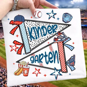 May include: A white graduation cap topper featuring two pennants with the text "KINDERGARTEN" in blue script. The design includes baseball-themed graphics like a cap, ball, glove, cleats, a hot dog, popcorn, a drink, and red and blue stars.
