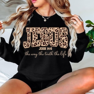May include: Black sweatshirt featuring the word "JESUS" in a leopard print pattern. The text "JOHN 14:6" and the phrase "the way the truth the life" are below the word "JESUS" in a script font.